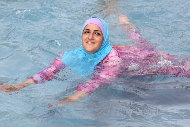 epa03366113 A young Turkish woman cools off while wearing a burkini at an open-air bath in Berlin, Germany, 20 August 2012.  EPA/STEPHANIE PILICK